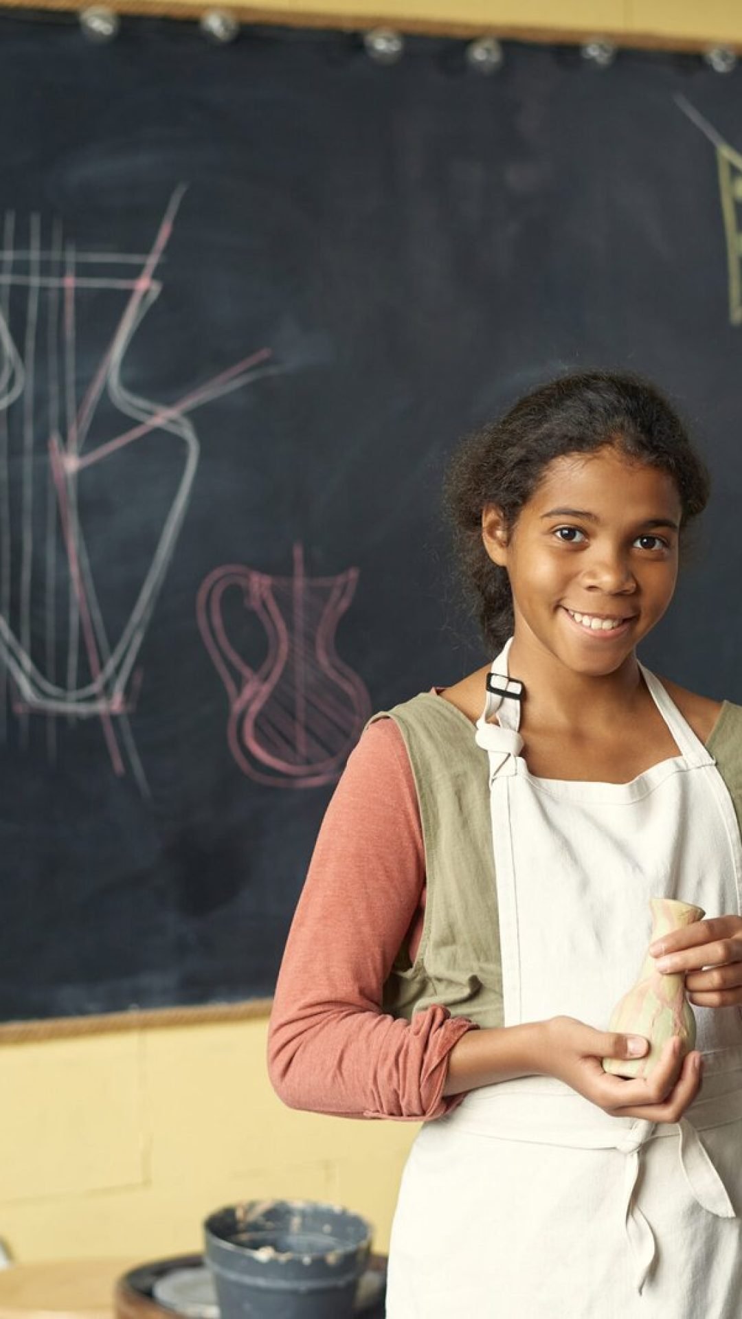 happy-cute-schoolgirl-with-clay-pot-standing-by-bl-2023-11-27-05-15-40-utc-scaled.jpg